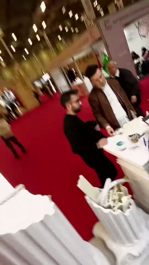 Fuar koridorunda ziyaretçiler ve yivli dekoratif sütun parçası görülüyor