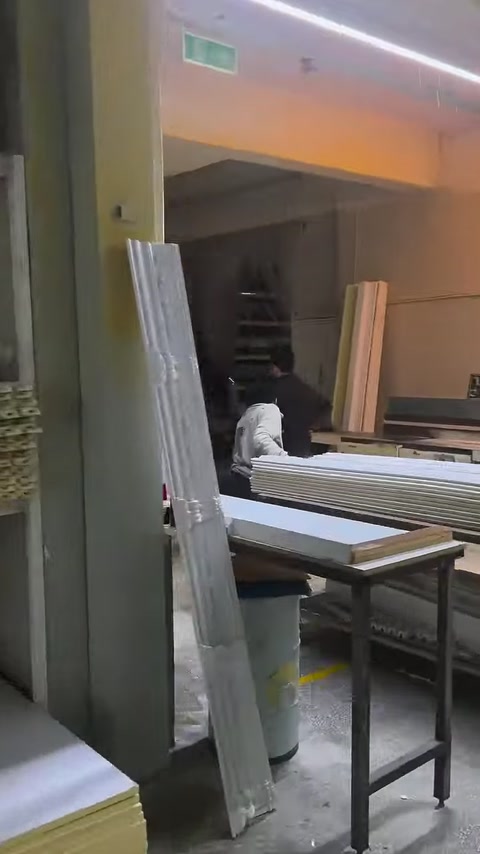 Usta, uzun beyaz dekoratif profilleri makine tezgâhında hazırlıyor.