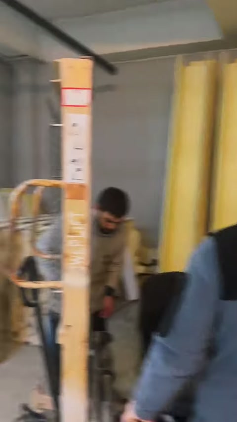 Çalışan, dik konumdaki uzun süsleme profilini atölye içinde taşıyor.