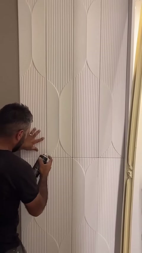 Montajcı dikey panel kenarına sprey uygularken yüzeyi eliyle destekliyor.