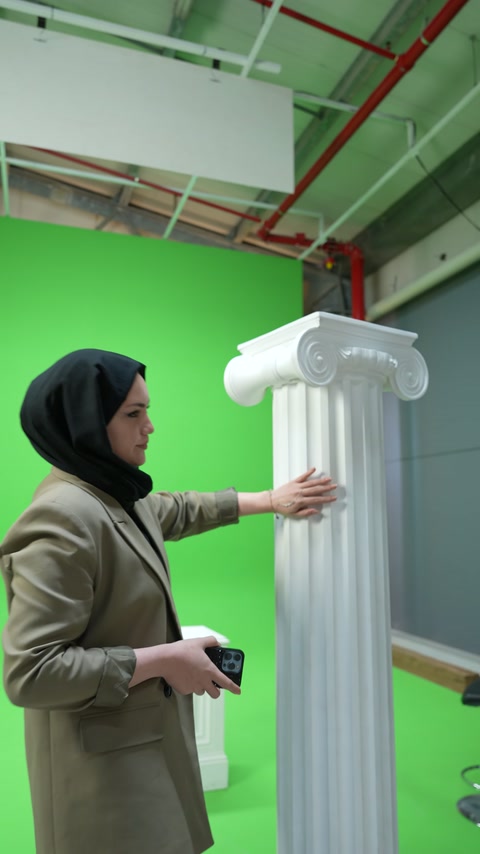 Kadın sunucu dik sütunun yivli yüzeyine eliyle işaret ediyor