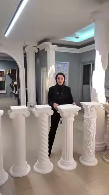 Sunucu, motifli başlıklara sahip üç beyaz sehpanın arkasında duruyor.