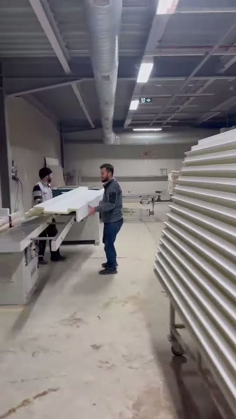 Bir usta atölye içinde uzun dekoratif profil taşırken görülüyor.