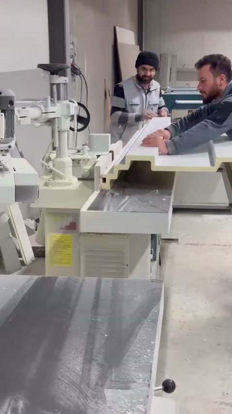 İki usta, profil parçasını kesim makinesi üzerinde birlikte konumlandırıyor.