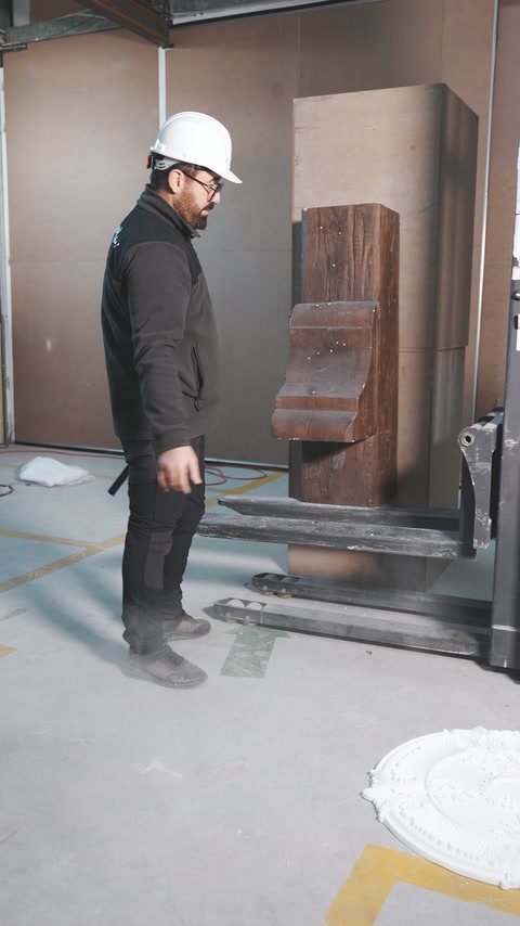 Baretli çalışan atölye zeminindeki kiriş parçasına doğru bakıyor.