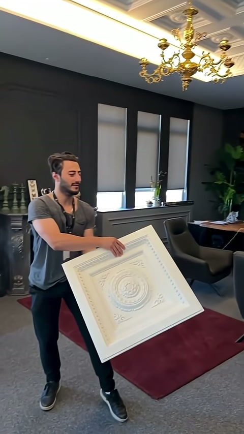 Sunucu dekoratif tavan panelini iki eliyle izleyiciye doğru tutuyor.