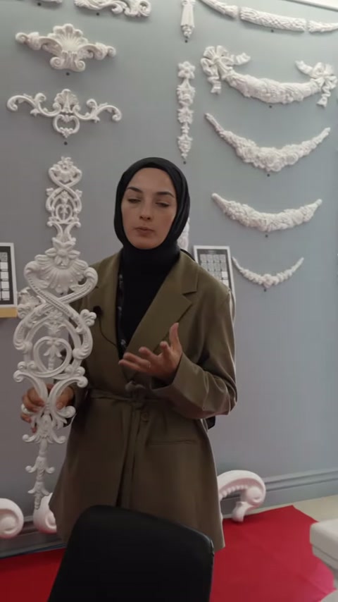 Kıvrımlı motif elde tutulurken farklı duvar süsleri arkada görülüyor