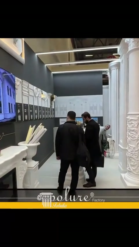 Klasik sütunların yanındaki koridorda ziyaretçiler duvar panolarını inceliyor