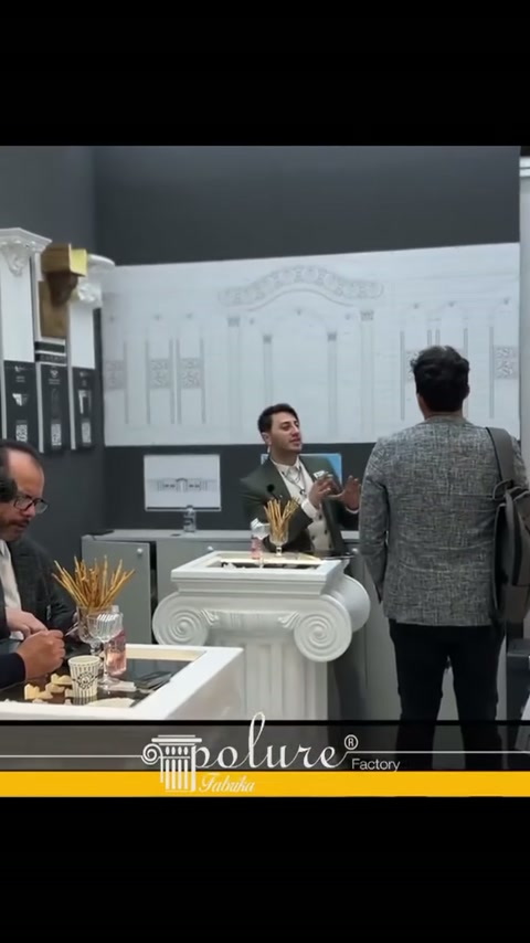 Stand görevlisi, dekoratif konsol yanındaki ziyaretçilere ürünleri anlatıyor