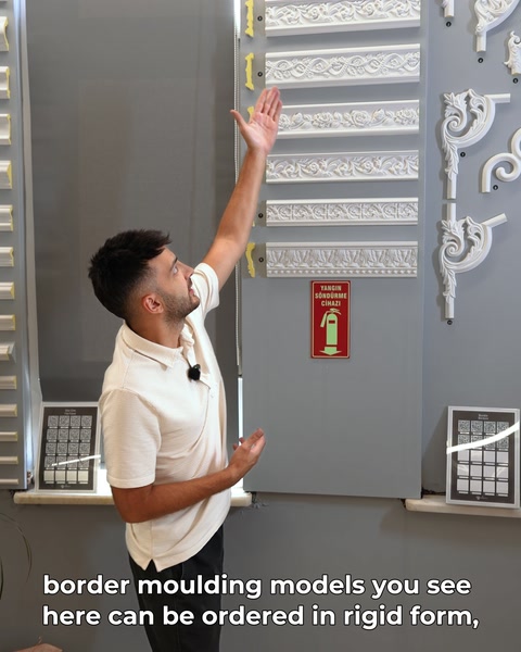 Kişi elini uzatarak duvardaki bordür modellerine işaret ediyor.