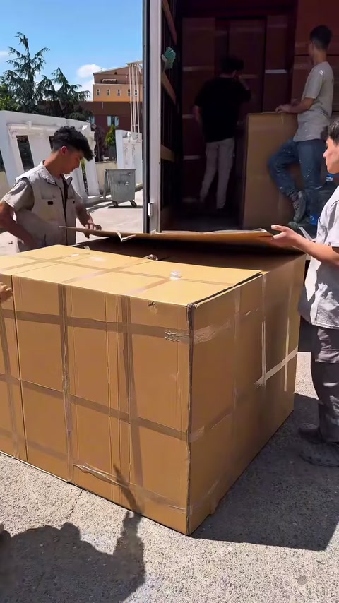 Bir çalışan kutu bağını çekerken diğerleri ambalajı tutuyor