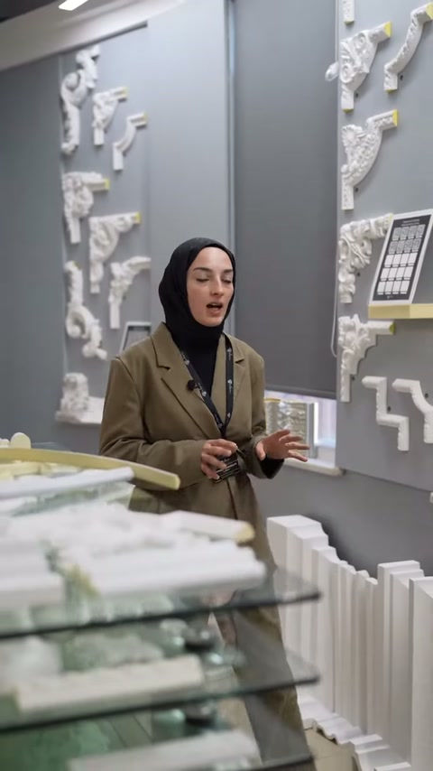 Cam tezgâhtaki süsleme parçaları önünde sunucu ürünleri açıklıyor.
