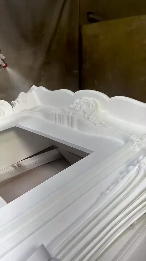 Beyaz şömine çerçevesinin kıvrımlı üst süslemeleri yakından görülüyor