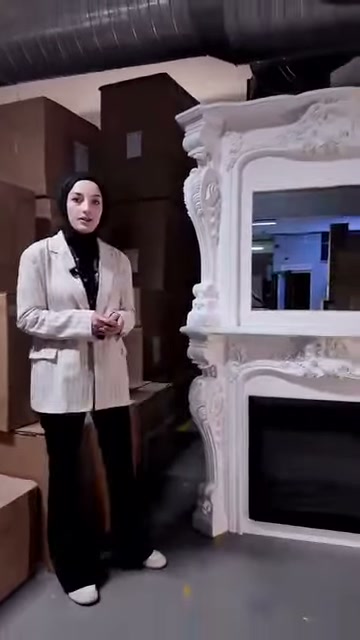 İşlemeli beyaz şömine çerçevesinin alt kısmında siyah hazne bulunuyor