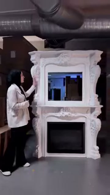 Sunucu şöminenin çiçek motifli üst köşesine eliyle dikkat çekiyor