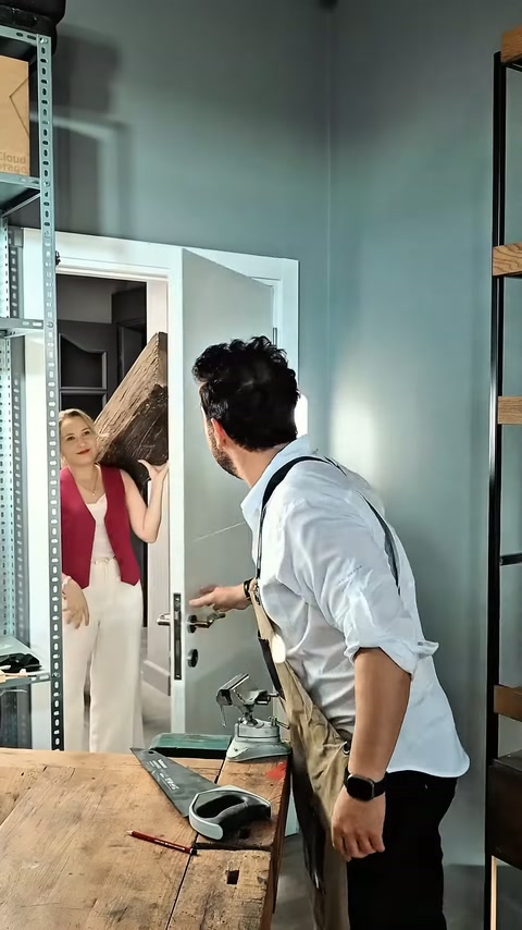 Kadın çalışan, atölye kapısında dekoratif kirişi erkek ustaya teslim ediyor.