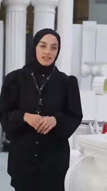 Sunucu, yüksek dekoratif sütunların önünde ellerini birleştirerek konuşuyor