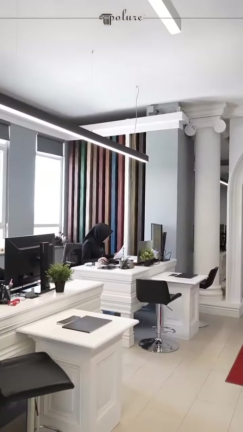 Beyaz sütunlar, ofis mobilyaları ve tavan aydınlatmaları birlikte görülüyor