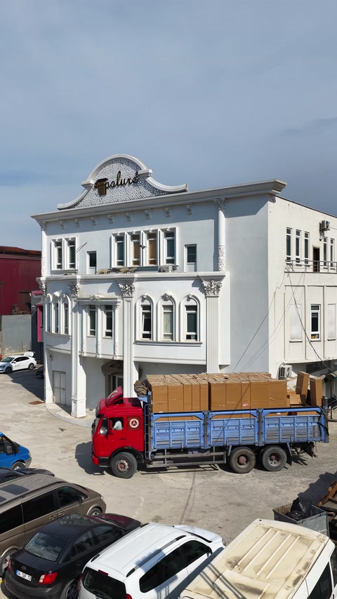 Süslemeli cephe önünde paketlenmiş ürünleri taşıyan kamyon görülüyor
